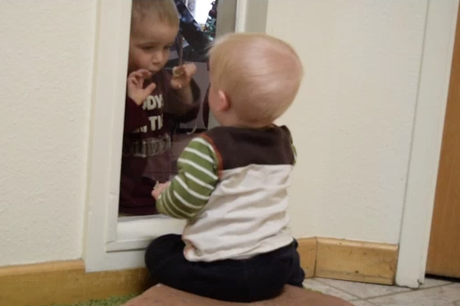 two one-year-old children interacting through a glass window